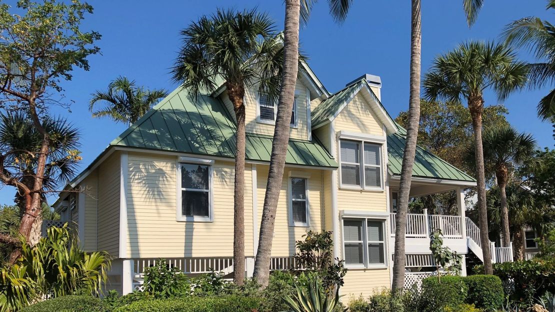 A yellow house with a green roof is surrounded by palm trees