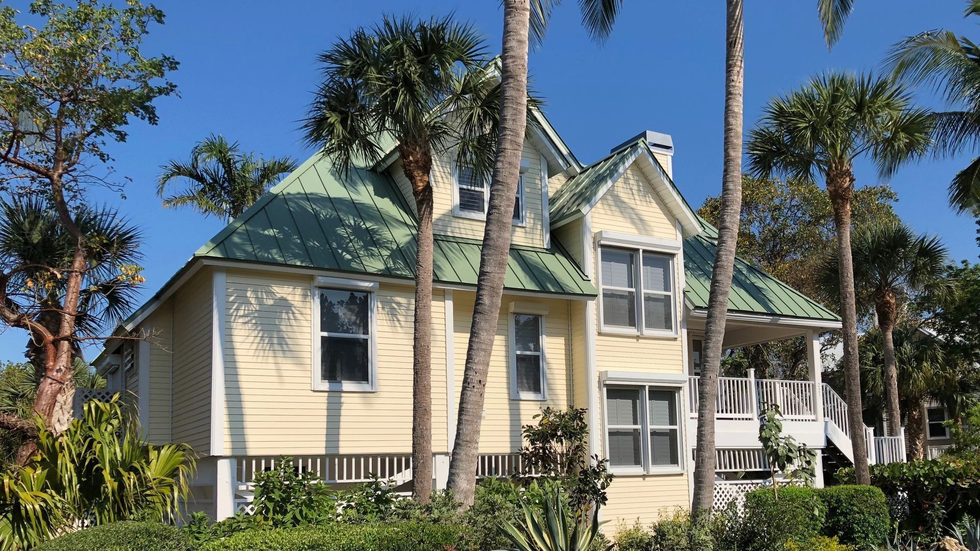 A yellow house with a green roof is surrounded by palm trees