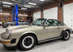 Beige classic Porsche 911 in a garage with a blue car lift in the background