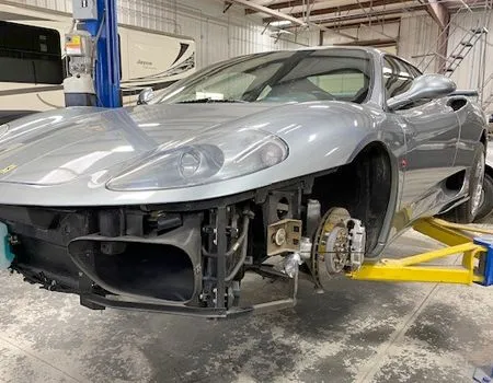 Silver sports car stripped on a lift in a garage, front bumper removed and front wheel off.