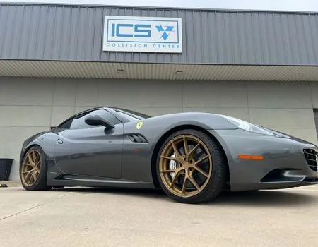 A dark gray Ferrari California with bronze wheels parked outside the ICS Collision Center.