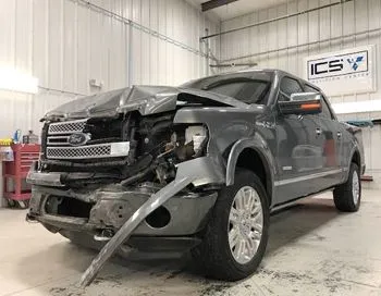 A ford f150 truck with a damaged front end is parked in a garage.