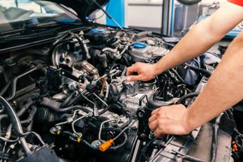 Mechanic's hands working on a car engine in a repair shop.