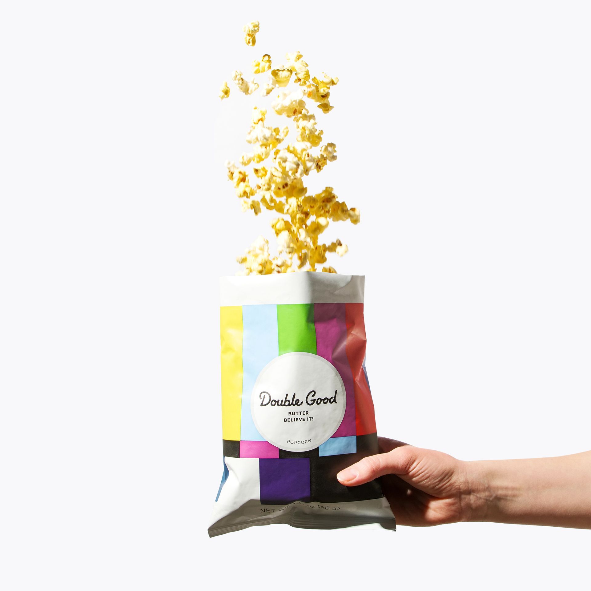 Hand holding a colorful popcorn bag with popcorn kernels bursting out.