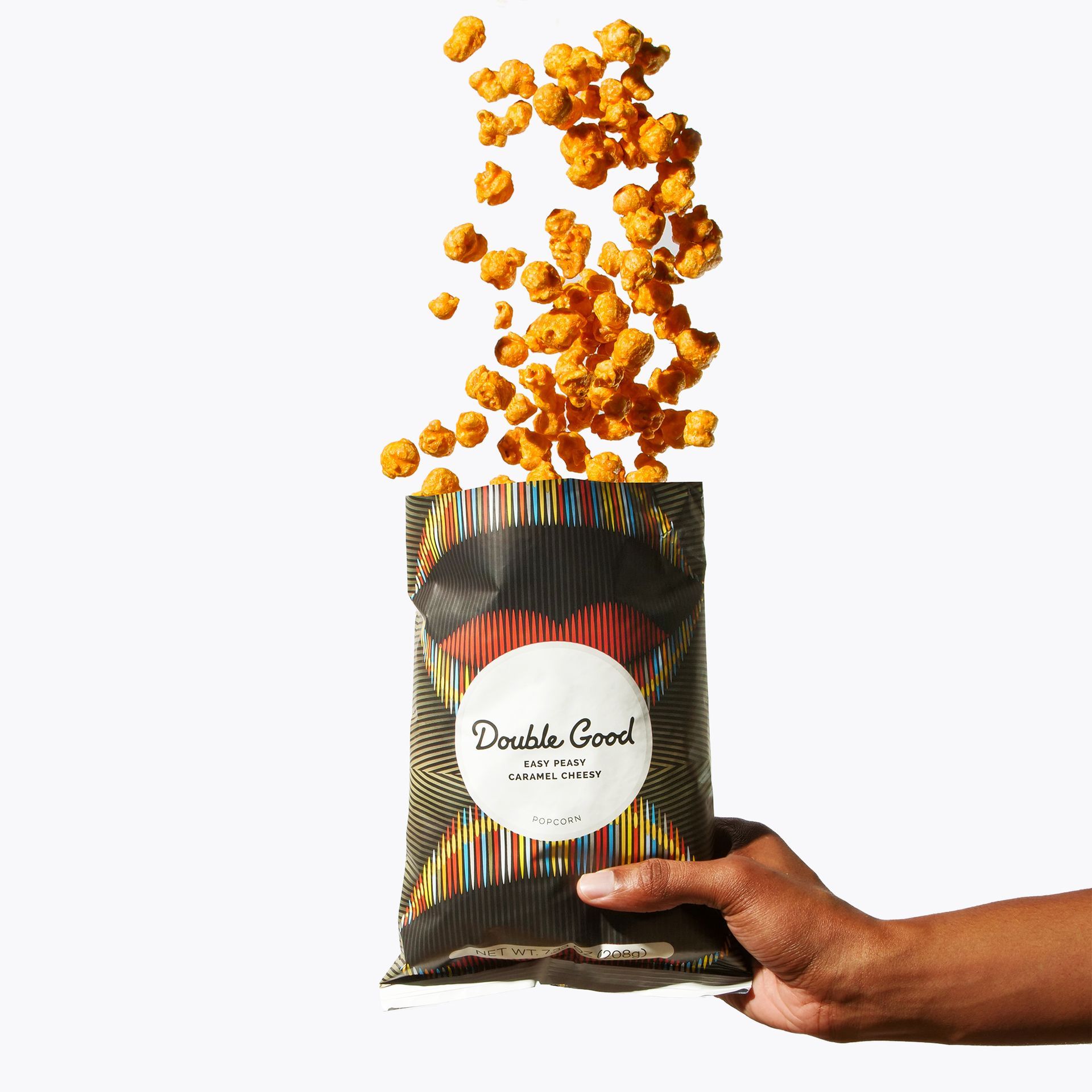 Hand holding a black bag of Double Good popcorn, popcorn kernels spilling out.