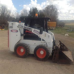 A bobcat skid steer loader is parked on the side of a dirt road.