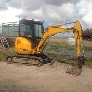 A small yellow excavator is parked on the side of a dirt road.