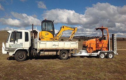 A white truck is towing a yellow excavator on a trailer.