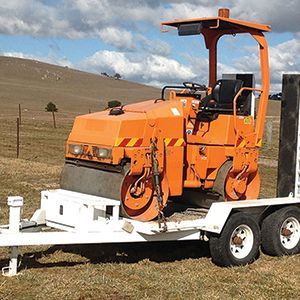 An orange roller is on a trailer in a field.