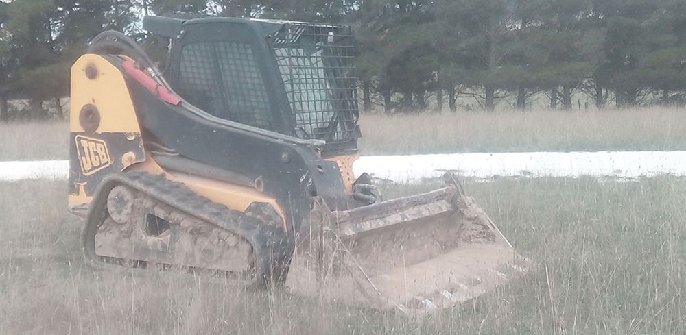 A bulldozer is driving through a grassy field in the rain.