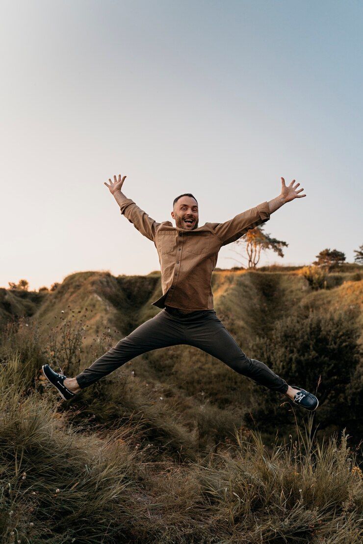 A man is jumping in the air in a field with his arms outstretched.