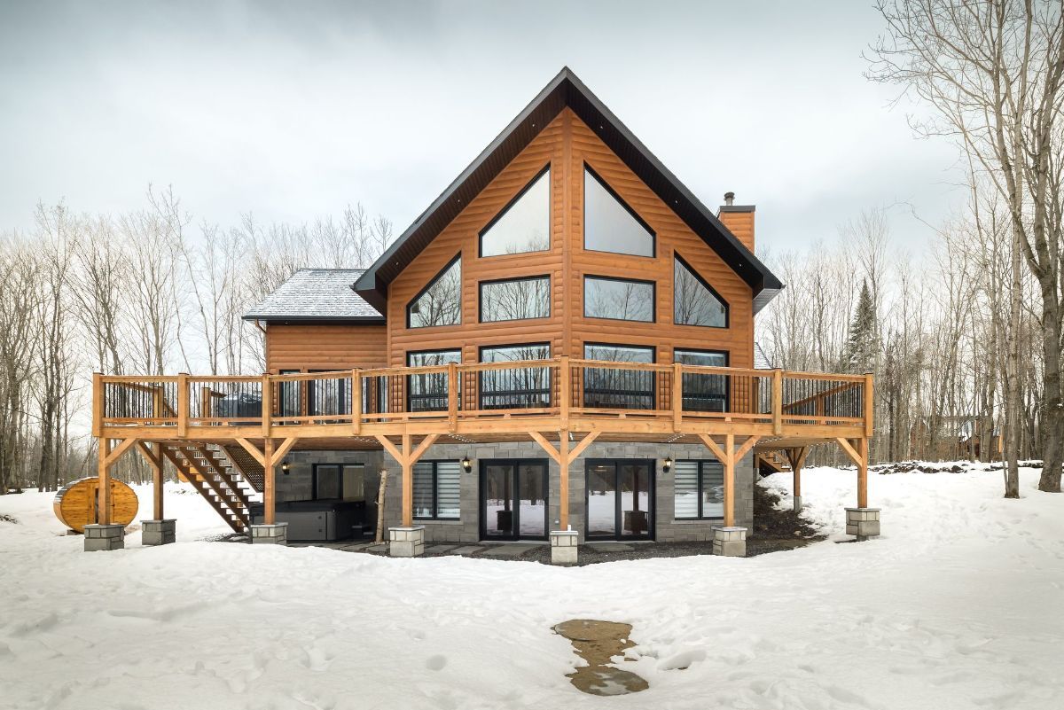 Large wooden cabin with a steep roof and decks, set in a snowy forest.