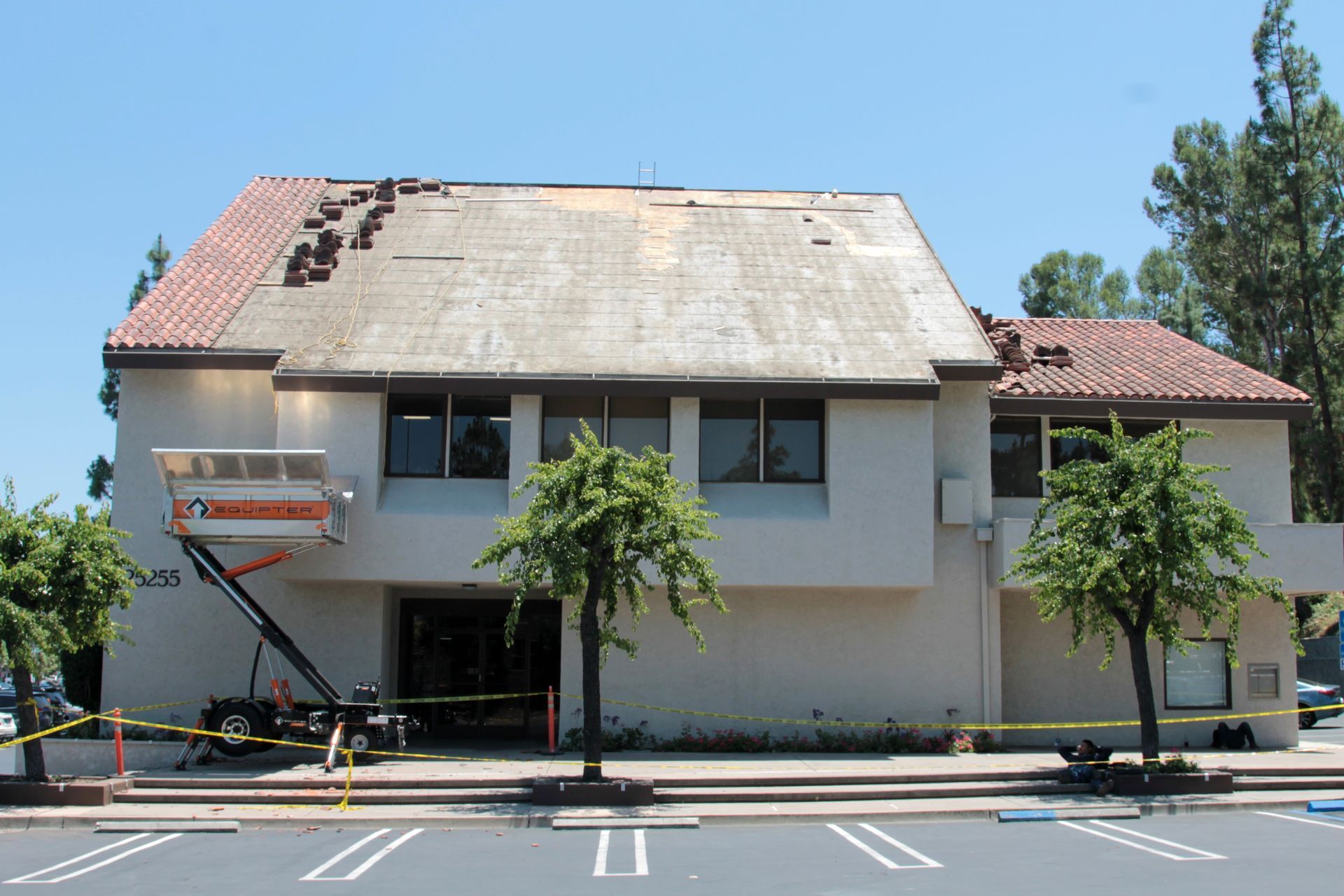 Two-story building with damaged roof and a lift truck parked in front on a sunny day
