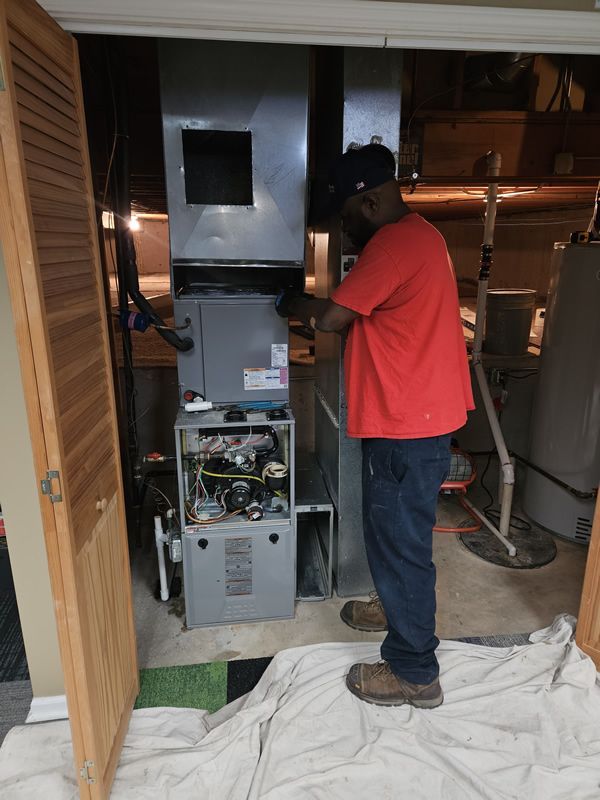 A man in a red shirt works on a furnace in a basement.