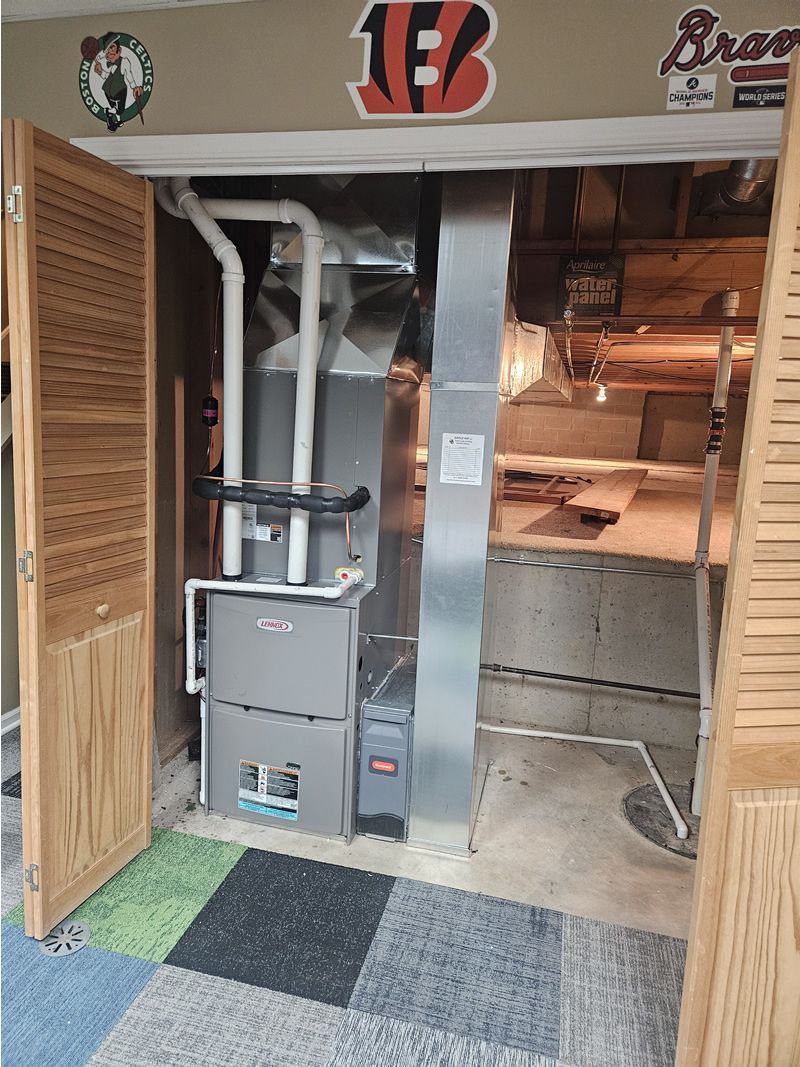 A furnace unit inside a utility closet, behind wooden folding doors, with sports logos above.