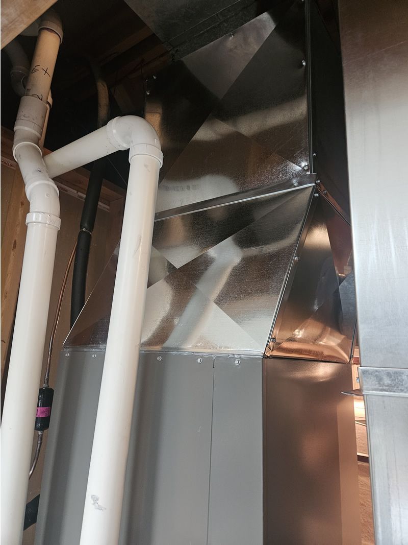 Metal HVAC ductwork with white PVC pipes in a basement setting.