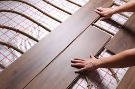 Hands installing wooden flooring over a radiant heat system, visible wires and silver foil.