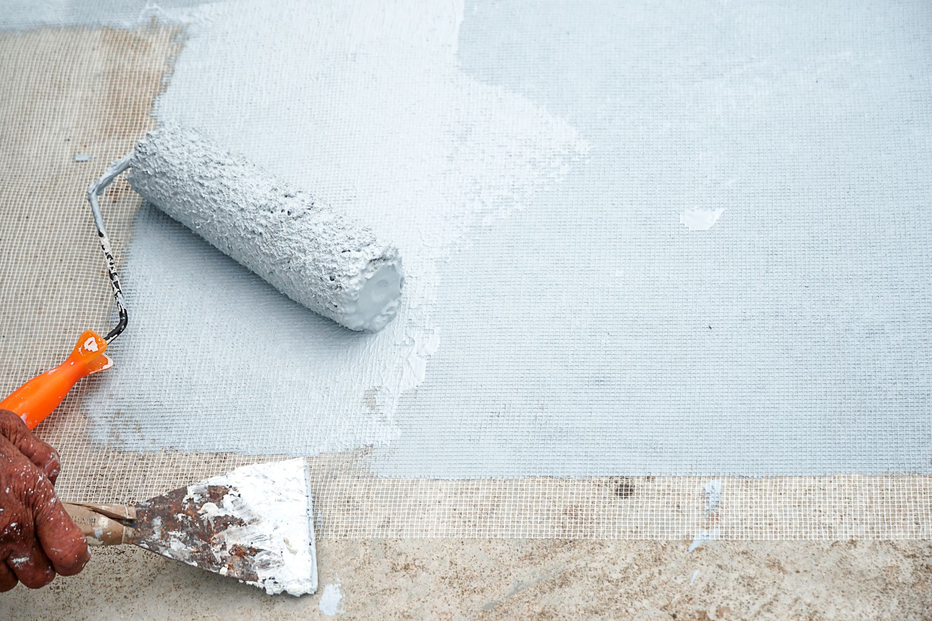 Paint roller applying waterproof coating over reinforcing mesh with trowel and sealant