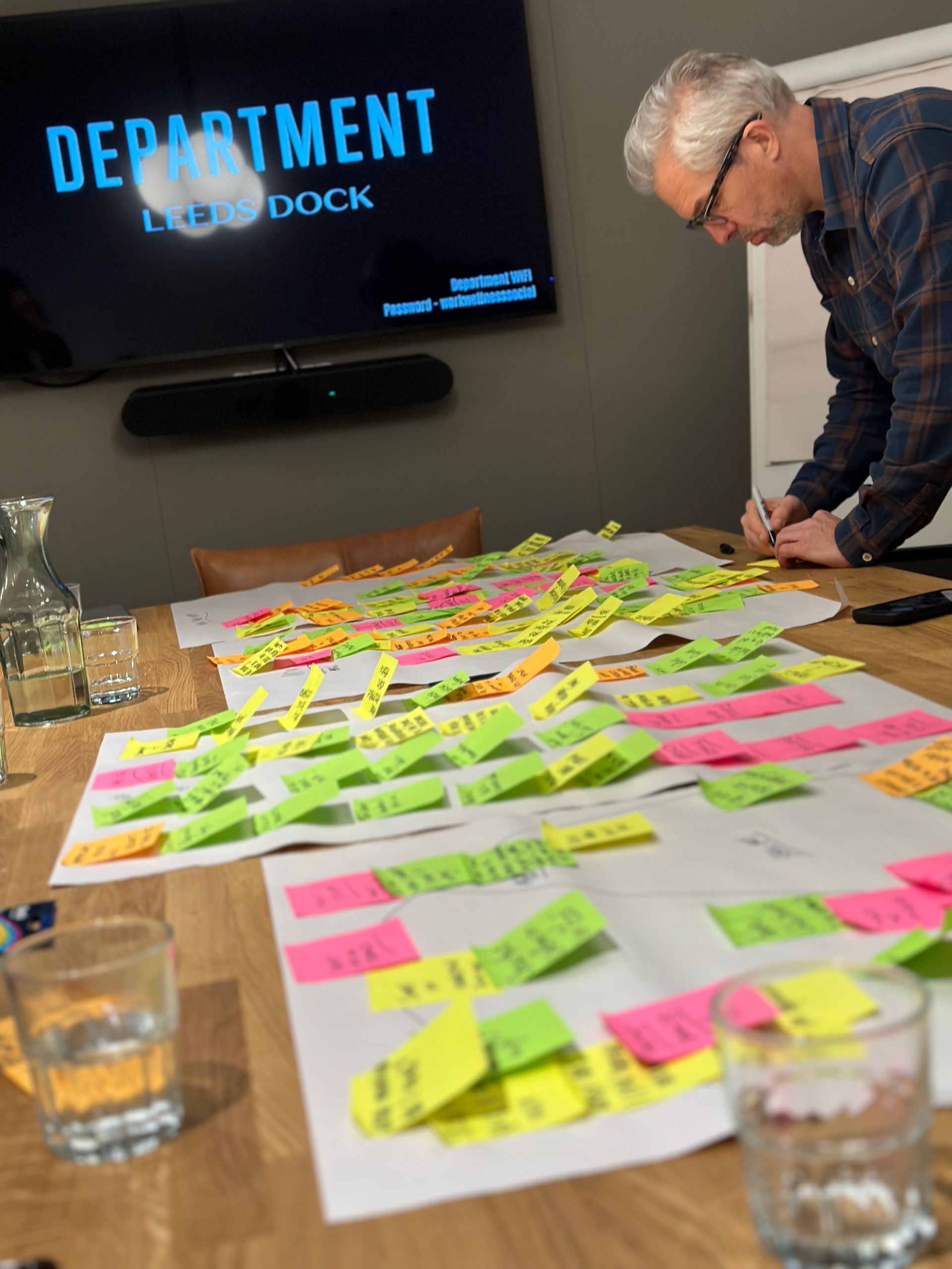 A man is writing on a piece of paper with sticky notes on it in front of a screen that says department