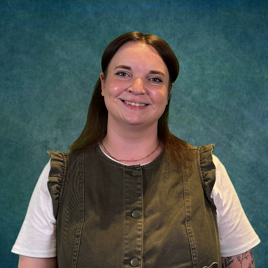A woman in a black shirt is smiling in front of a colorful brick wall.