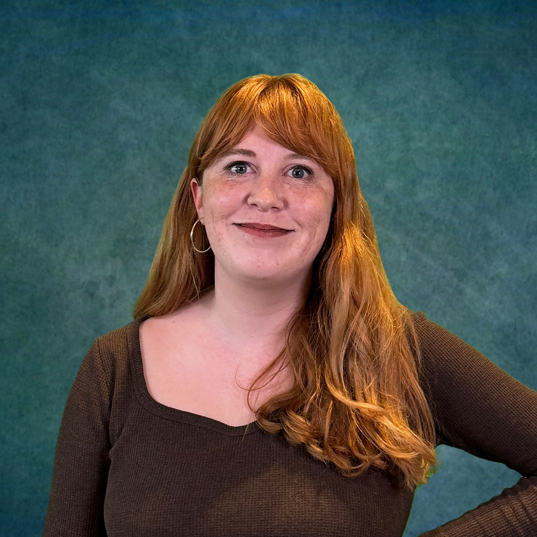 A woman with red hair is standing in front of a colorful brick wall.
