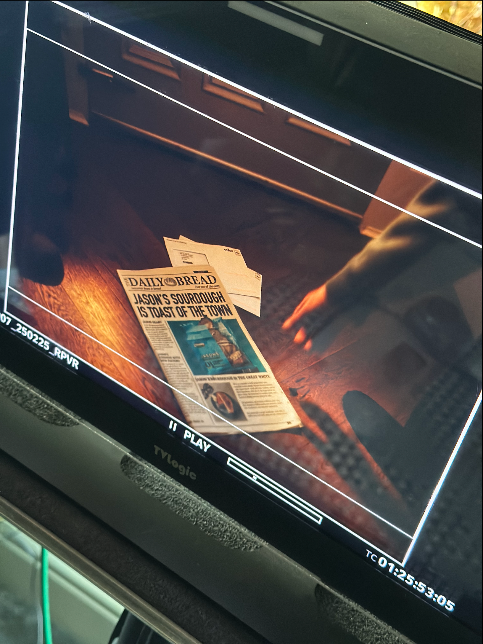 Monitor displaying a close-up of a newspaper and hand on a wooden surface, angled shot.