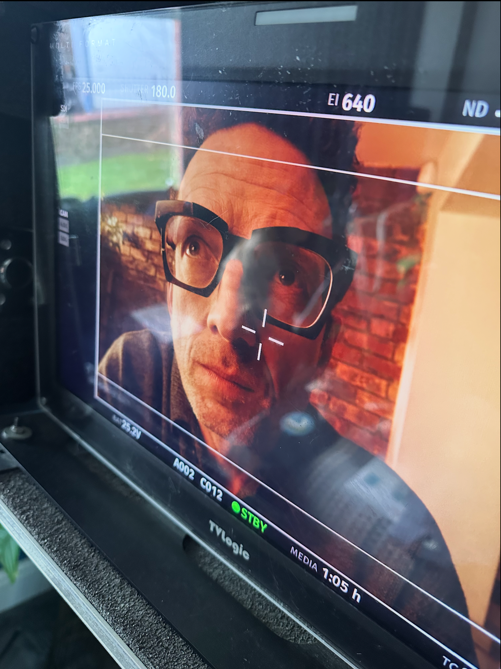 Person wearing glasses on a monitor screen, viewed from behind.
