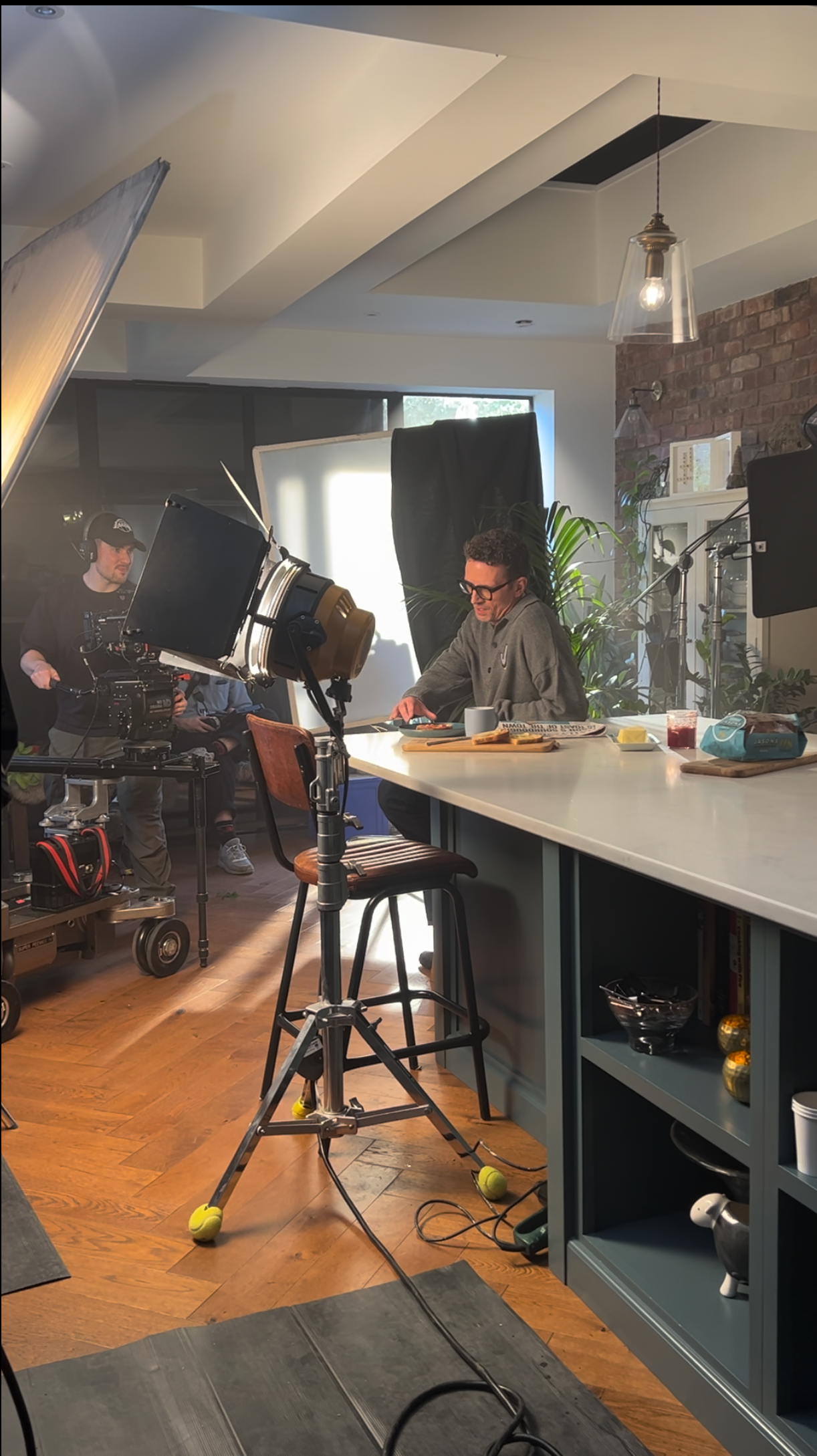 A person in a kitchen with film equipment, preparing food at a counter lit by professional lighting.