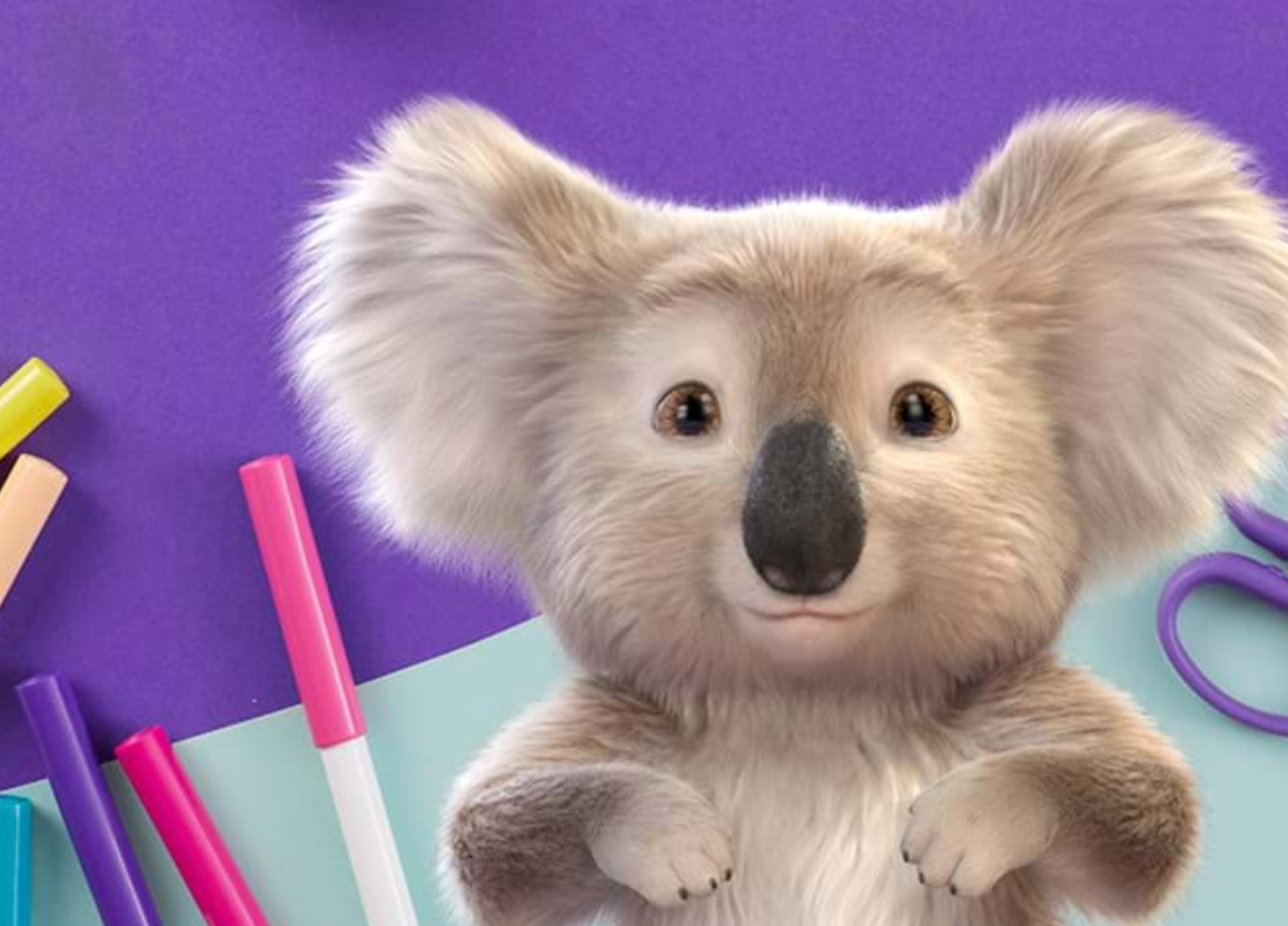 A stuffed koala bear is sitting on a table next to markers and scissors.