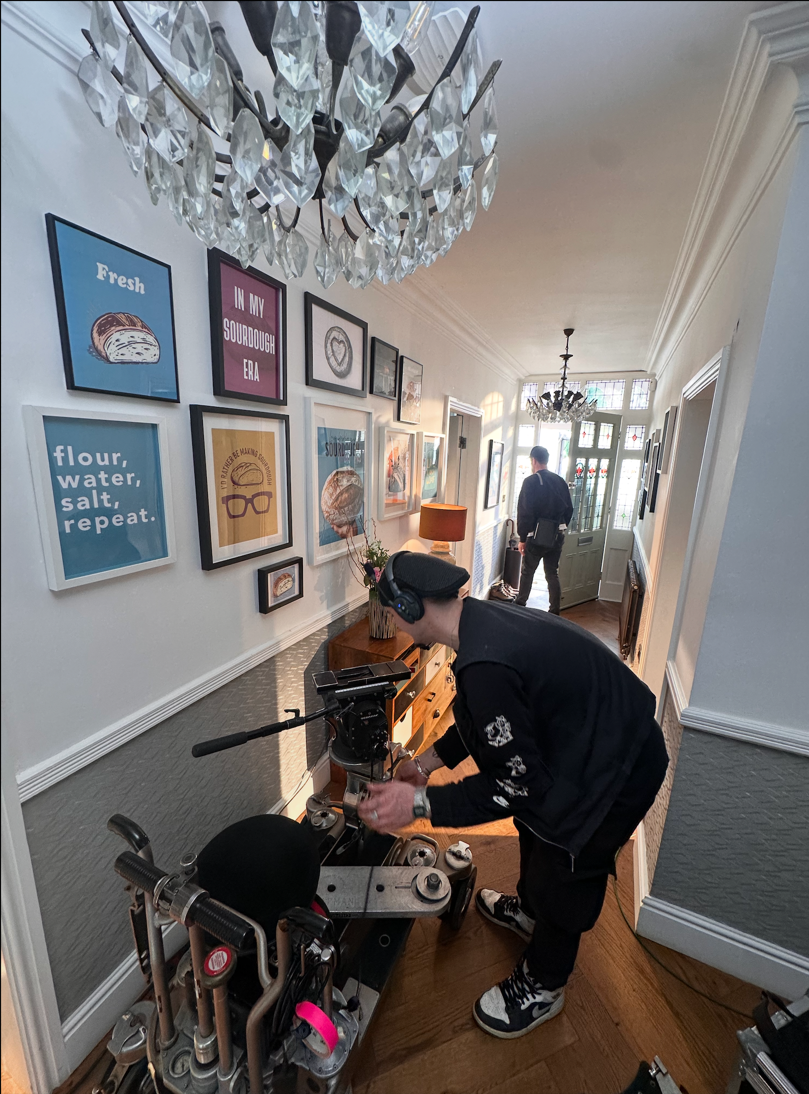 Person in black uniform adjusting a small vehicle in a hallway with art on the walls and a chandelier.