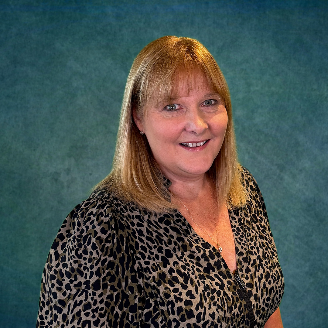 A woman in a leopard print shirt is smiling in front of a colorful wall.