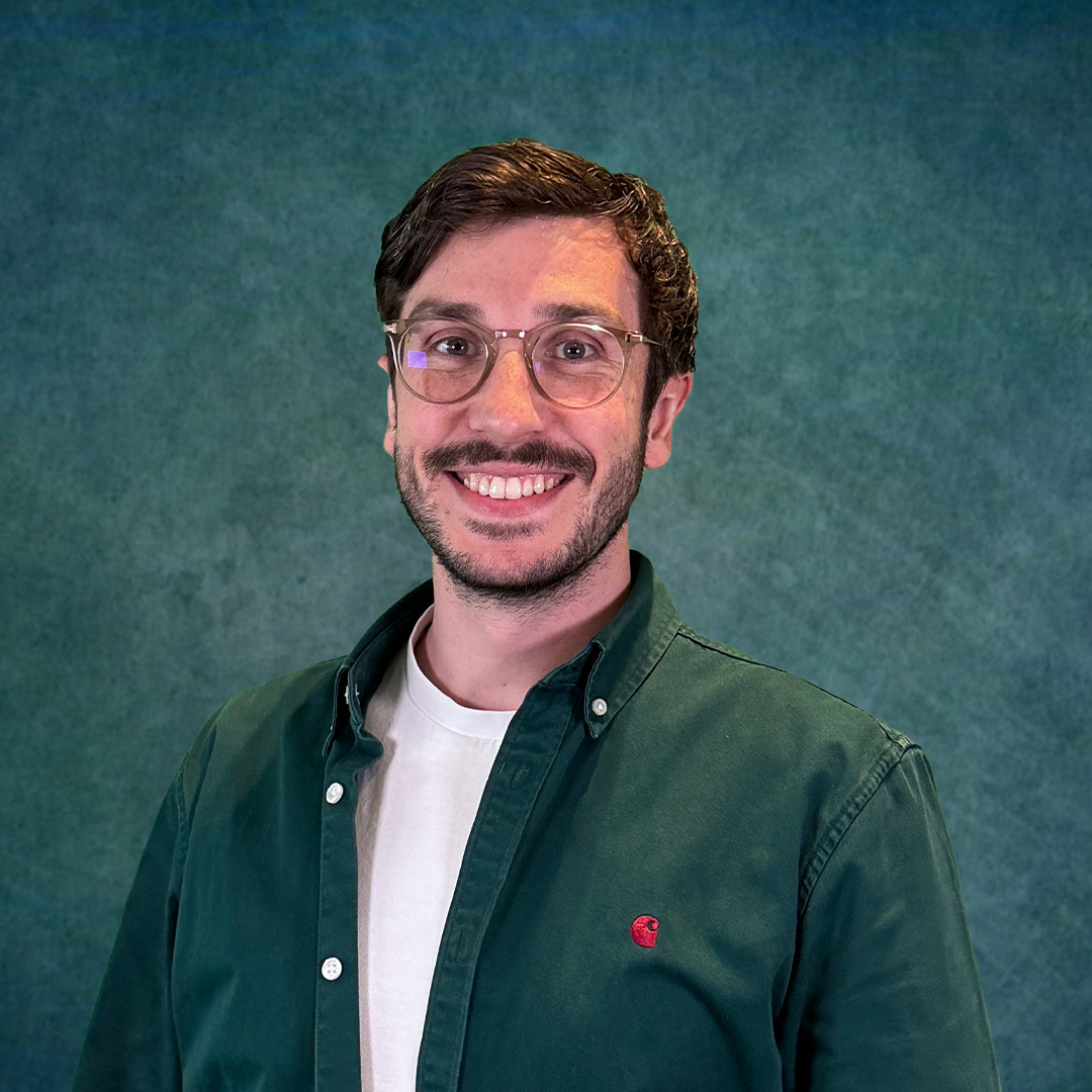 A man with glasses and a beard is standing in front of a colorful brick wall.