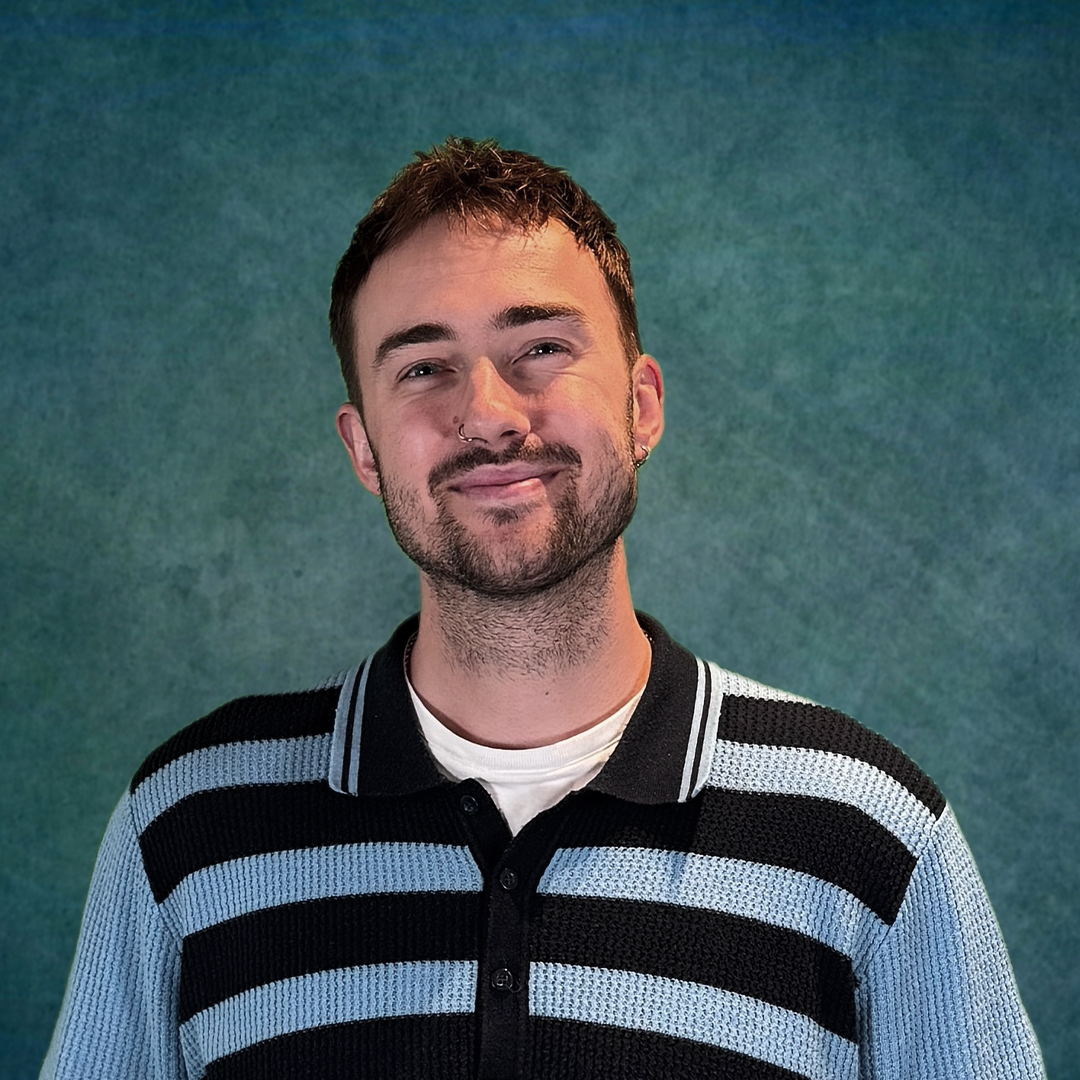 A man in a sweater is smiling in front of a colorful brick wall.