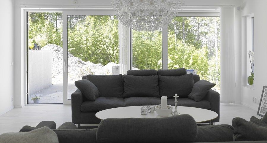 A minimalist living room with a dark grey sofa, white coffee table, and large windows looking out onto a wooded area.