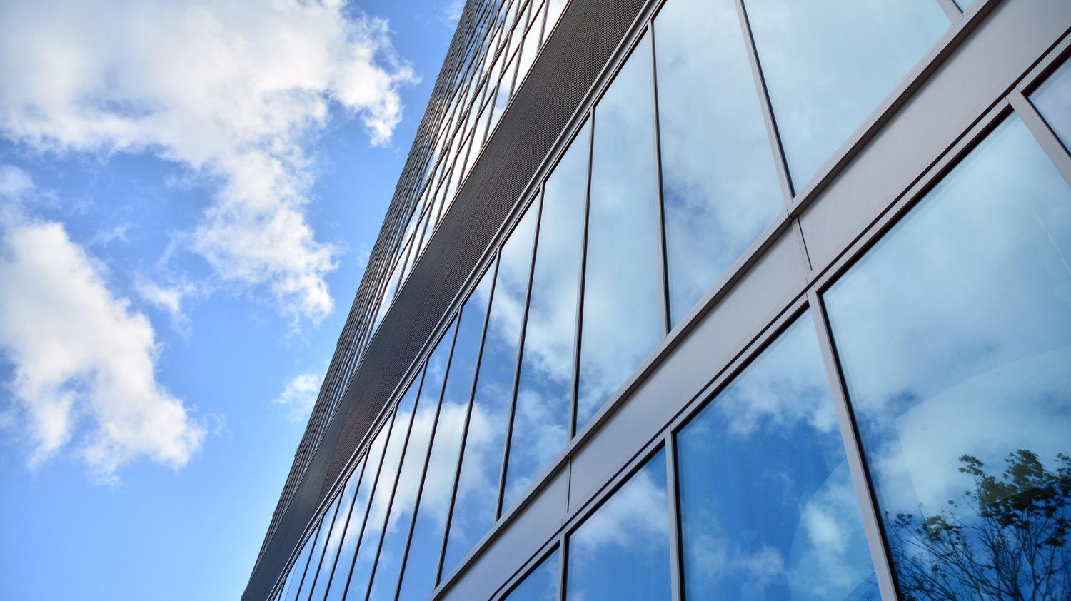 Modern glass office building reflecting blue sky and clouds