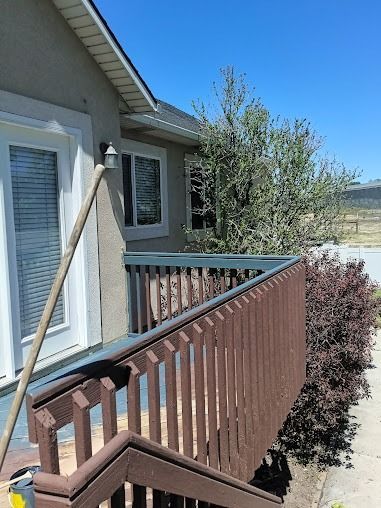 Brown wooden deck railing beside a gray house, overlooking a sunny desert landscape