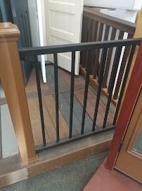 Black stair gate across a doorway with an open white door and carpeted floor nearby