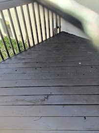 Dark gray wooden deck with vertical railings and greenery beyond the steps