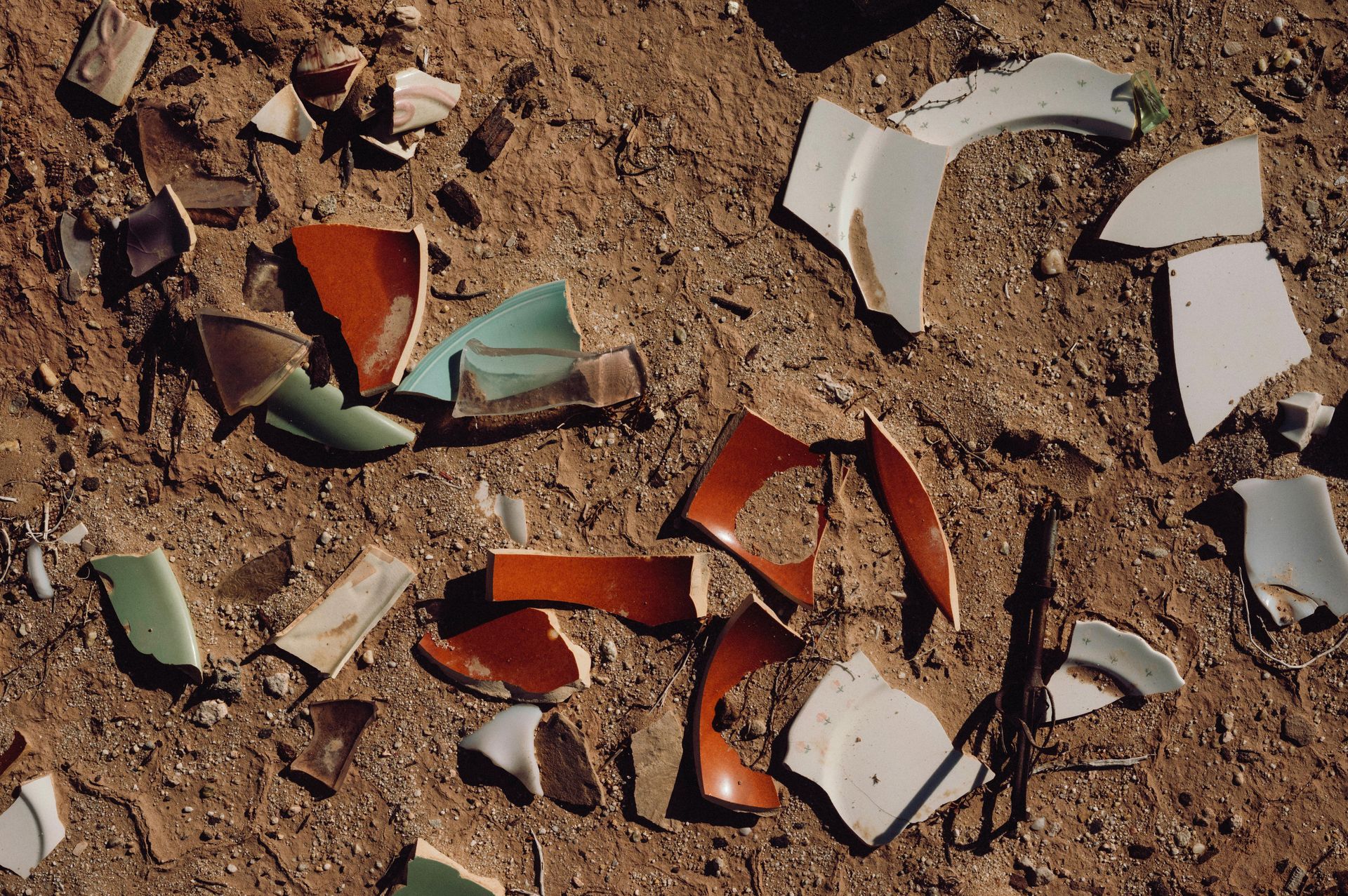Broken colorful ceramic shards scattered on dry dirt ground
