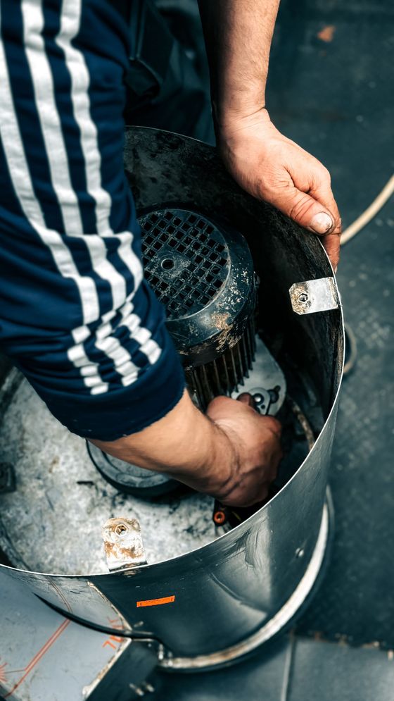 Hands working inside a metal bucket, removing or arranging a black object with tools.