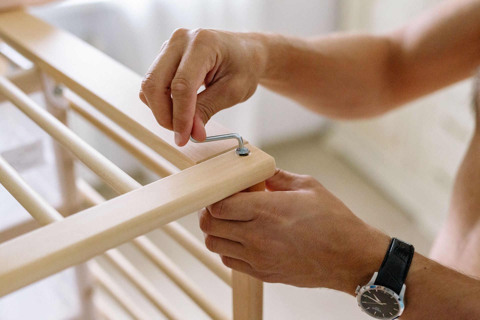 Hands assembling a light wooden frame with screws using a screwdriver, close-up.