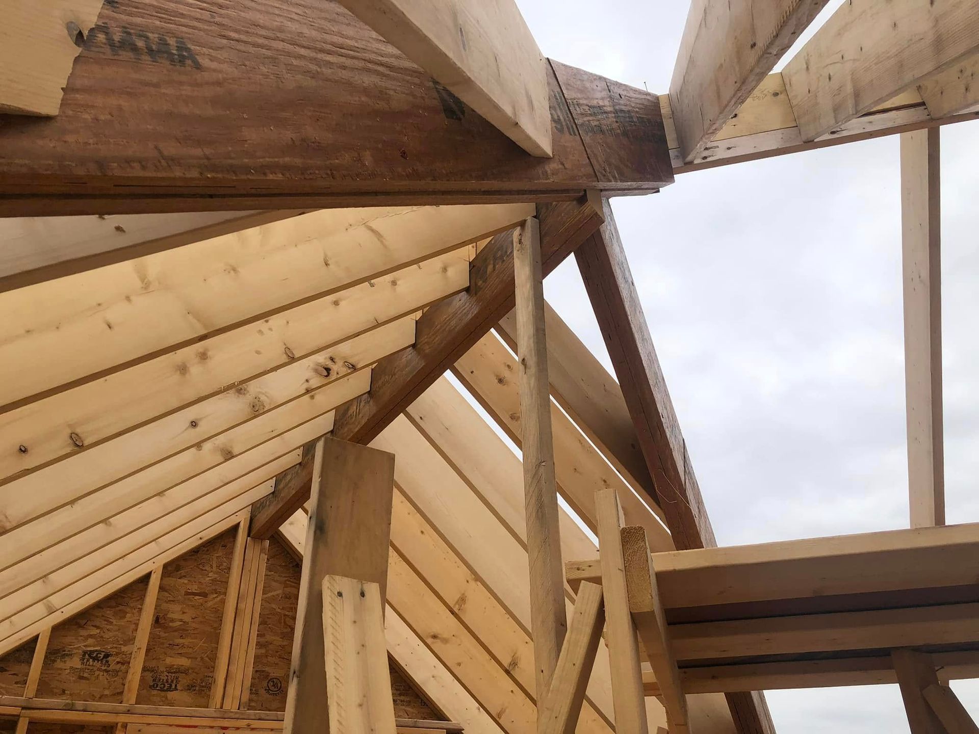 Wooden roof framing under construction against a cloudy sky.