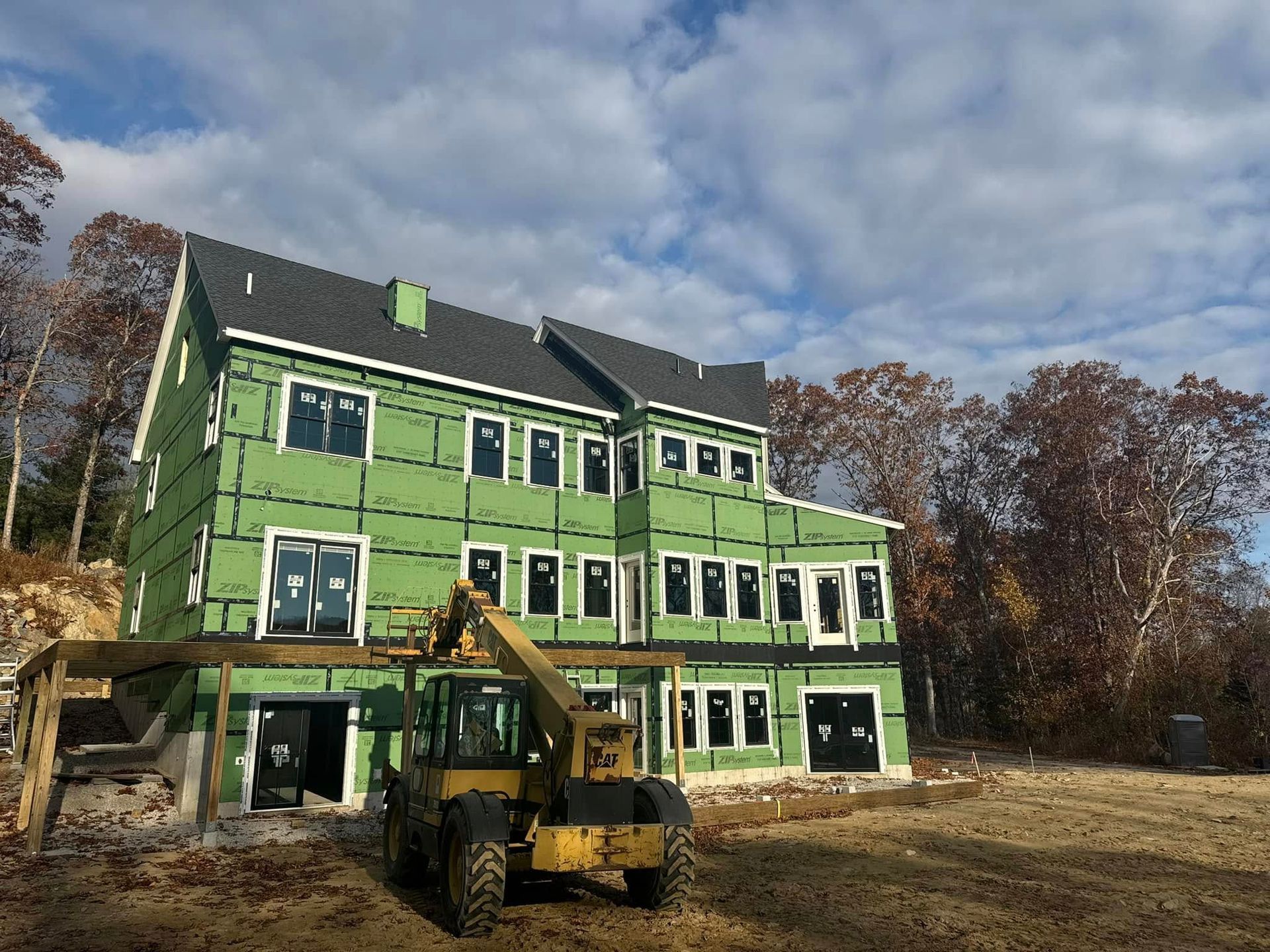 Building under construction; green siding, black roof, yellow tractor on site.