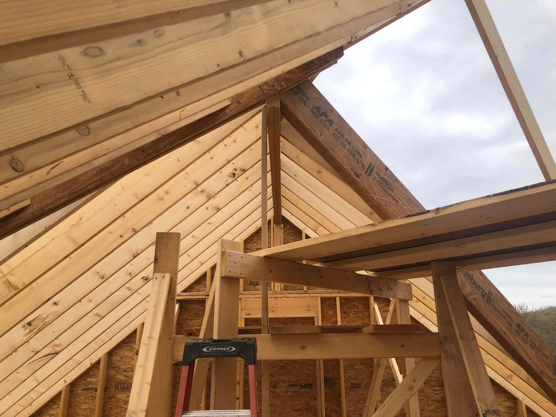 Wooden roof framing under construction against a cloudy sky.