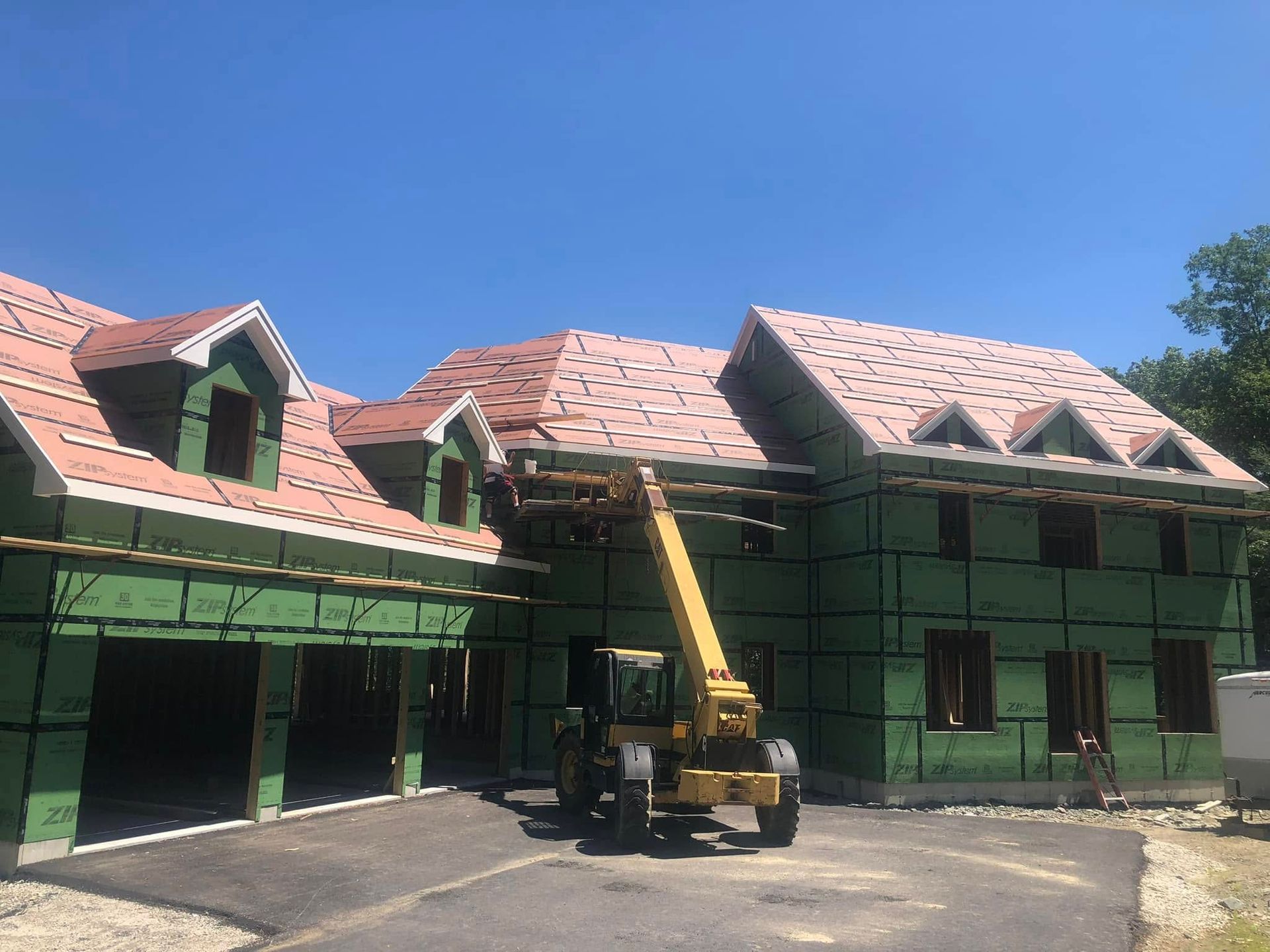 Construction of a two-story house with a yellow forklift in front, on a sunny day. Green walls, red roof.