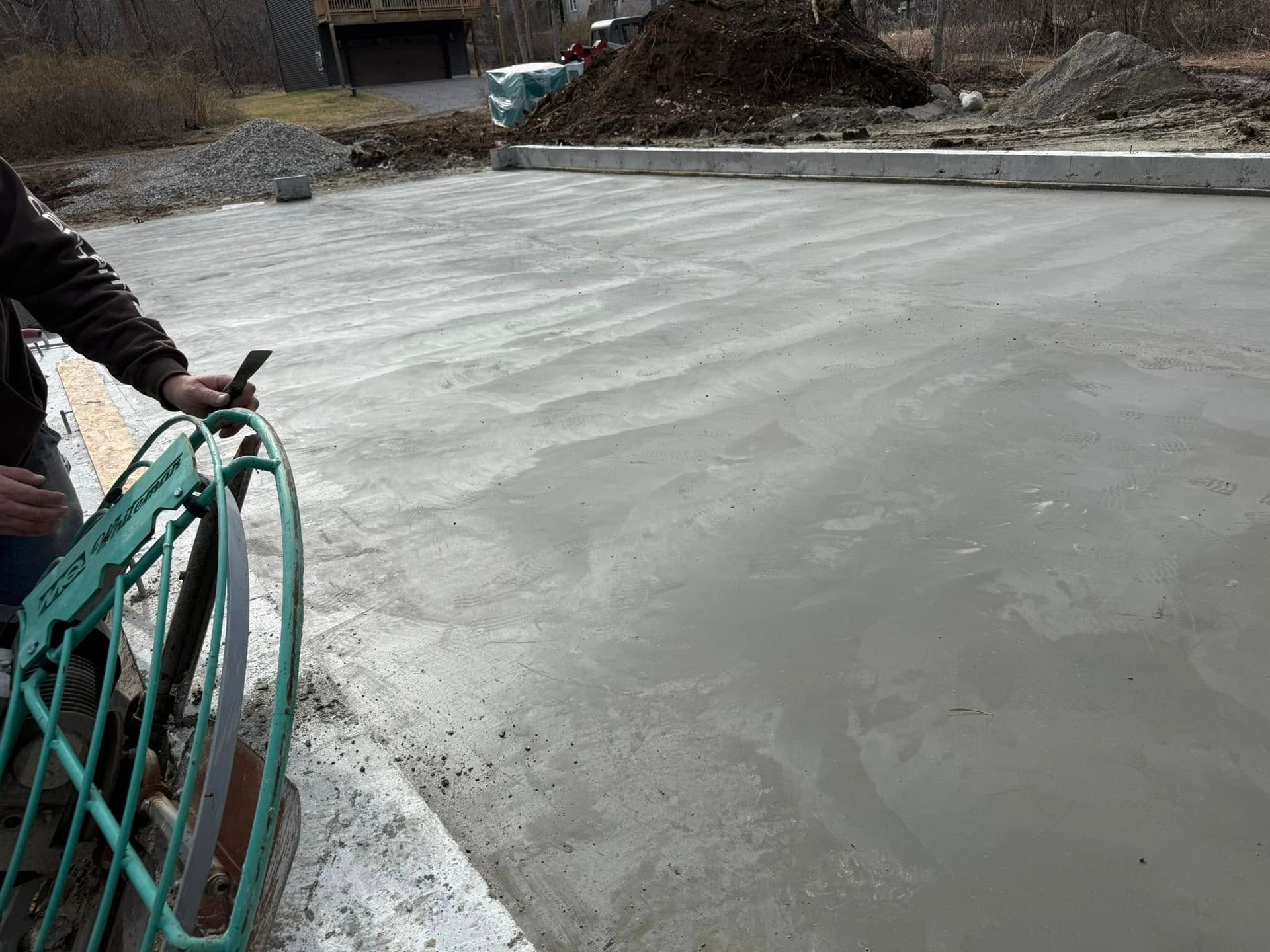 Person smoothing wet concrete with a tool; recently poured concrete surface.
