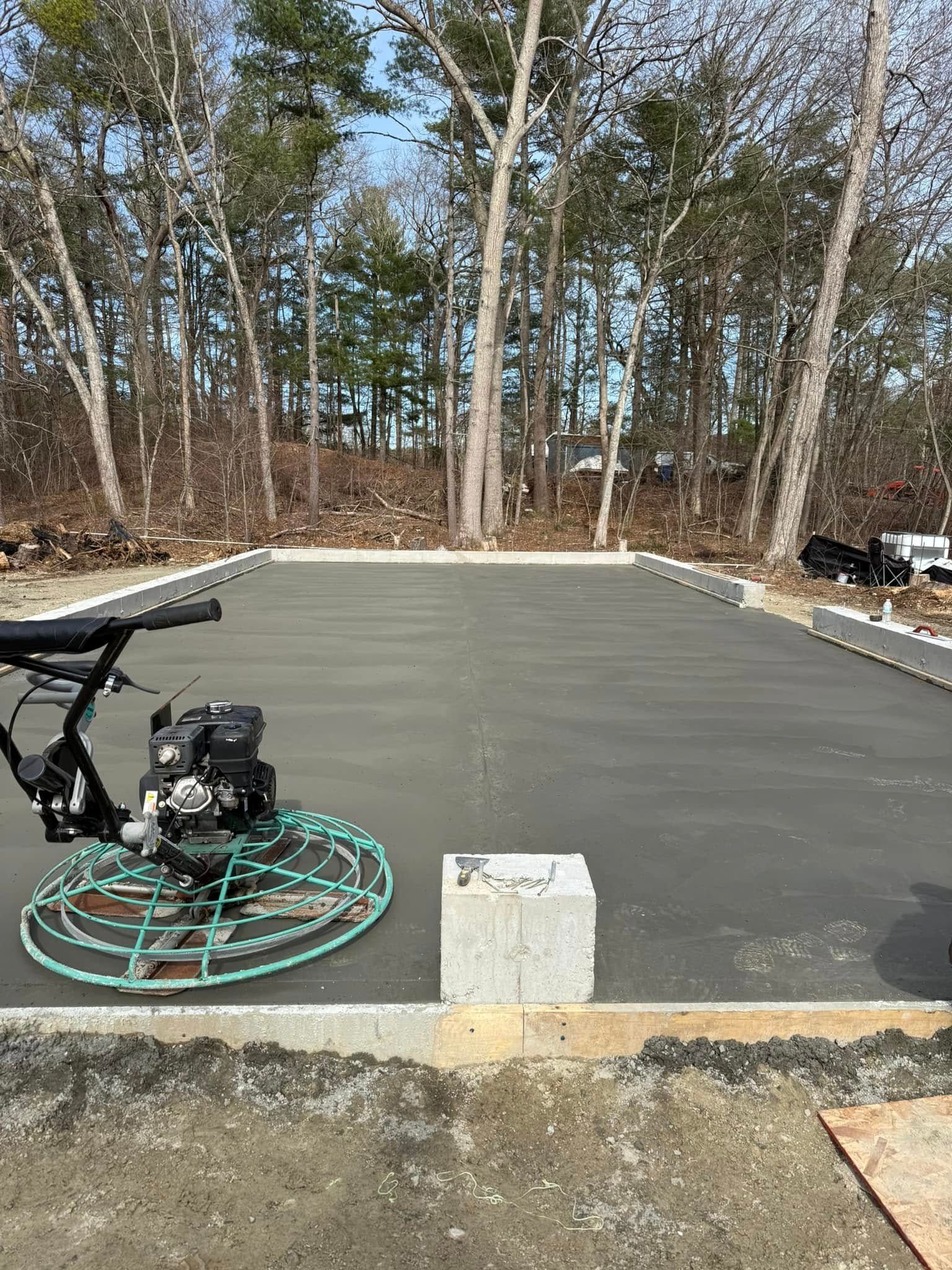 Freshly poured concrete slab with power trowel. Outdoors, trees in background, sunny day.