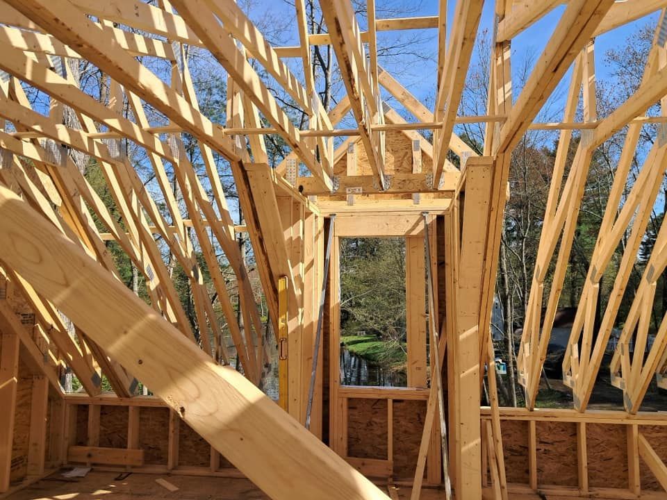 Wooden framework of a building's roof and walls, with an opening for a door, outdoors on a sunny day.