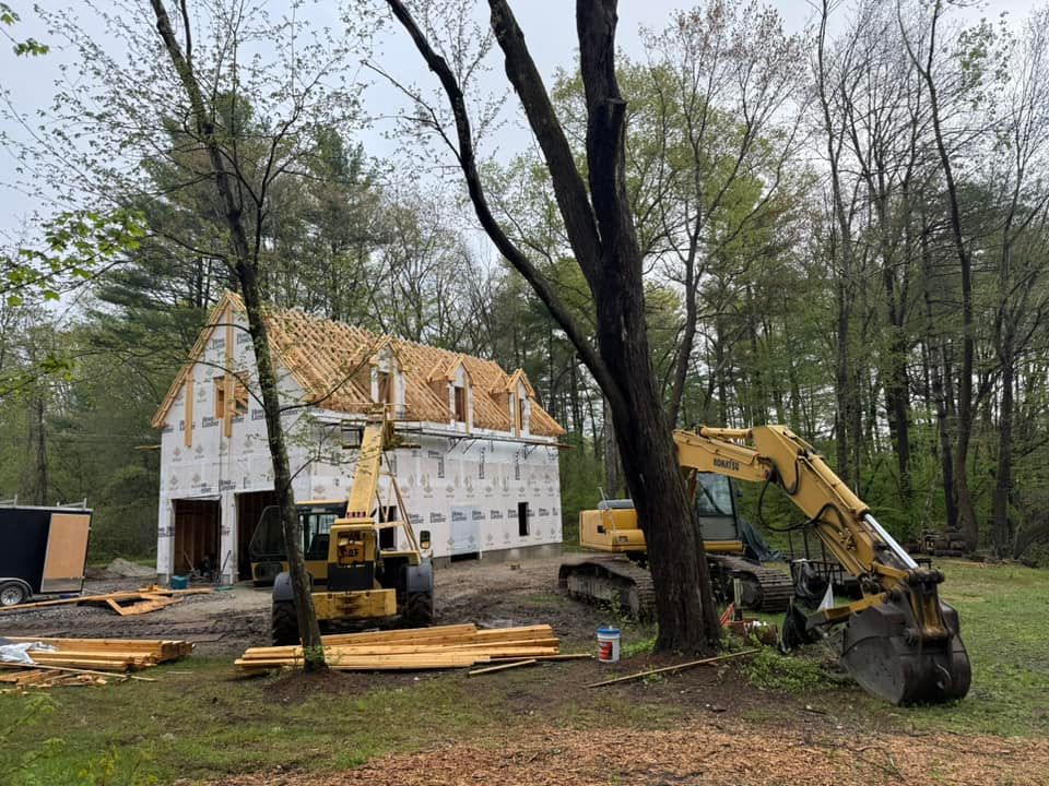 Construction site with a building, excavator, and other machinery surrounded by trees.