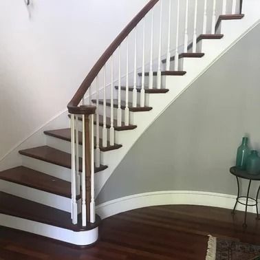 Curved wooden staircase with white balusters, dark wood handrail and steps, against a gray wall.